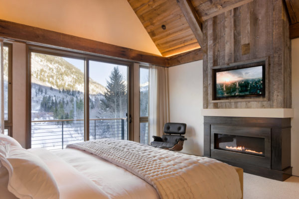 a rustic mountain-styled bedroom has a steel plate linear fireplace and reclaimed barnwood with tv above