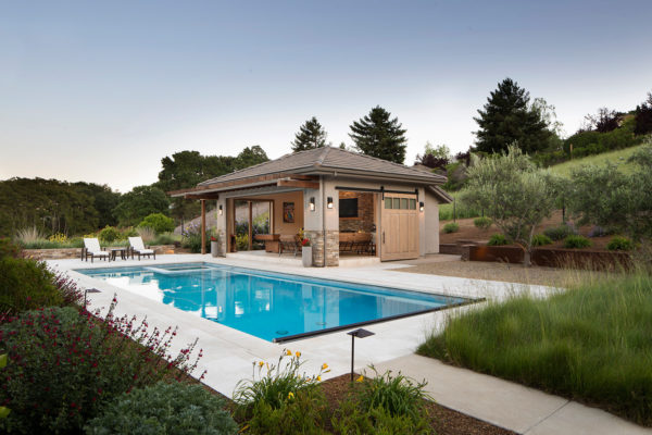 a transitional backyard amidst natural landscape featuring a modern pool and open-air pool house with bathroom