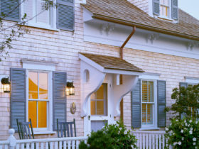 go for a charming exterior featuring a roof over door entry, gray clapboards, and white fence