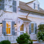 go for a charming exterior featuring a roof over door entry, gray clapboards, and white fence