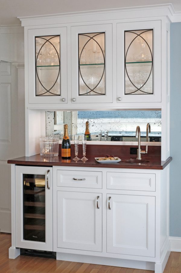 an elegant yet small wet bar features a mahogany countertop and white cabinets
