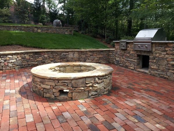 pair the natural stone retaining wall fire pit with red brick flooring for a classic and traditional patio