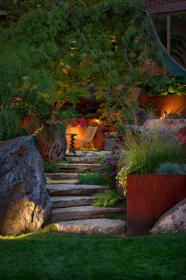 use dramatic lighting to elevate this industrial backyard and its stunning landscaping slopes with rocks