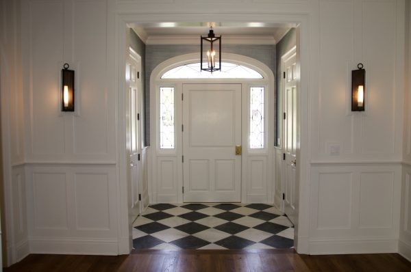 an elegant entryway featuring a white front door, farmhouse chandeliers, and black and white floor