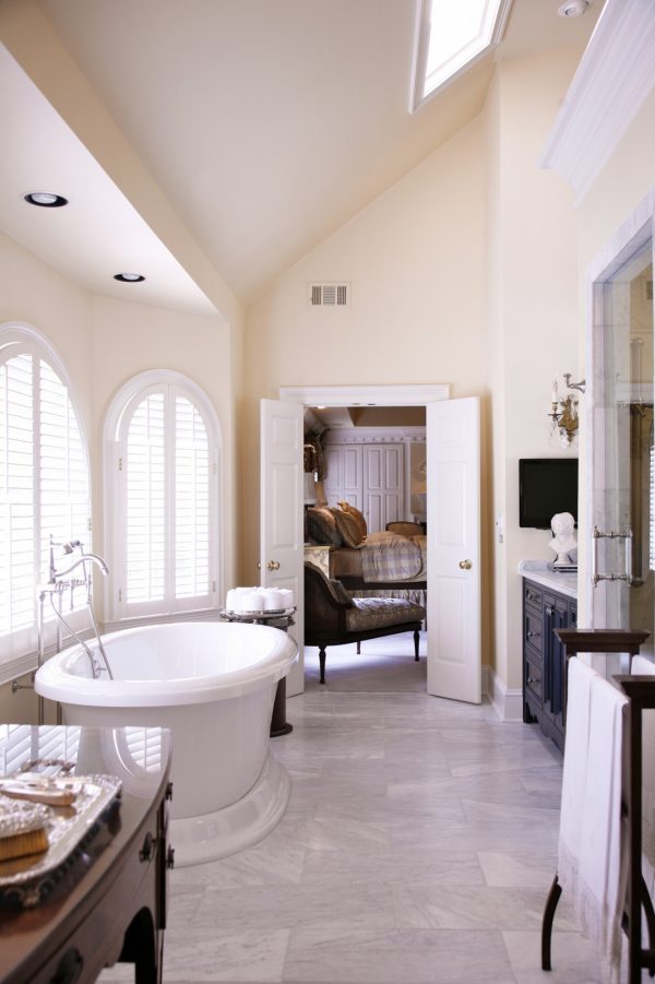 elevate an elegant master bathroom with white shutters on arched windows and marble tile floors