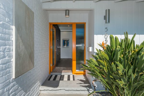 nod to 1960s design with this orange front door and lush planters for a private entryway