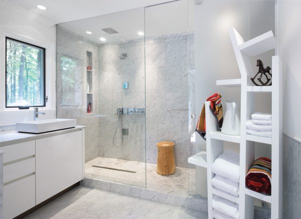 this carrara marble shower has a tall built-in shelf that complements the chic white color palette
