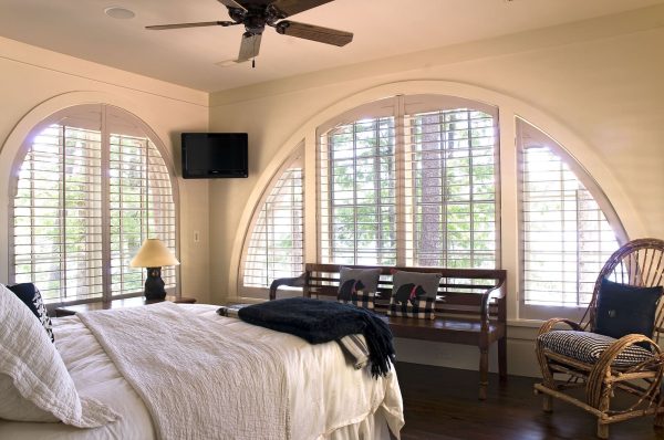 use custom wood shutters for dramatic arched windows to highlight the stunning architecture in a bedroom