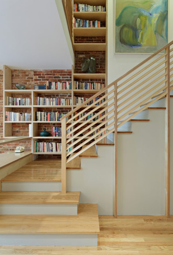 this indoor diagonal wood stair railing design features a mini library for a dramatic entryway
