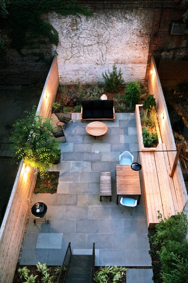 this small backyard with no grass uses bluestone pavers and wood walls for a trendy city garden