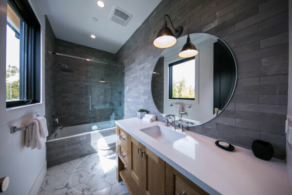 a round mirror and light wood shaker cabinets can enhance a rustic, mountain styled dark grey bathroom