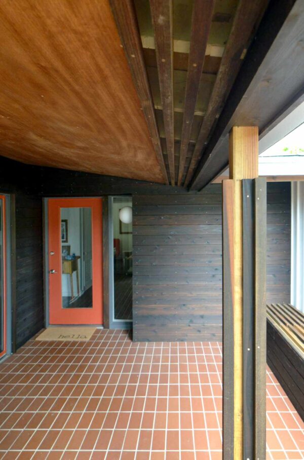 brown front porch quarry tile offers a midcentury charm against the red front door and wood siding