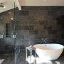 create a rustic dark grey bathroom with charcoal limestone tiles and a country wood cabinet