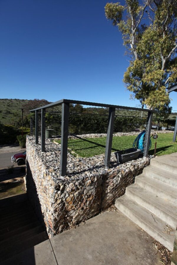 erect black railing fence on retaining wall made of gabion stone for a modern landscape ambiance