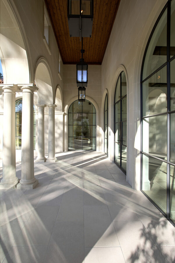 this front porch uses limestone tile and arched glass windows to evoke a mediterranean vibe in a modern way