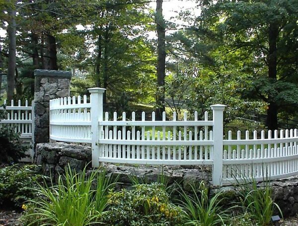 this white chestnut hill fence follows the curvature on the retaining wall for a stunning arch and beautiful backyard
