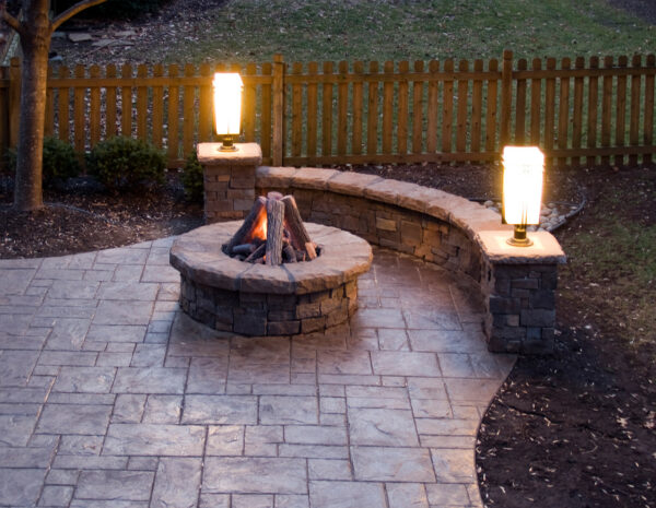 use azek decking and warm lighting for a comfy stamped concrete patio with fire pit and stone walls